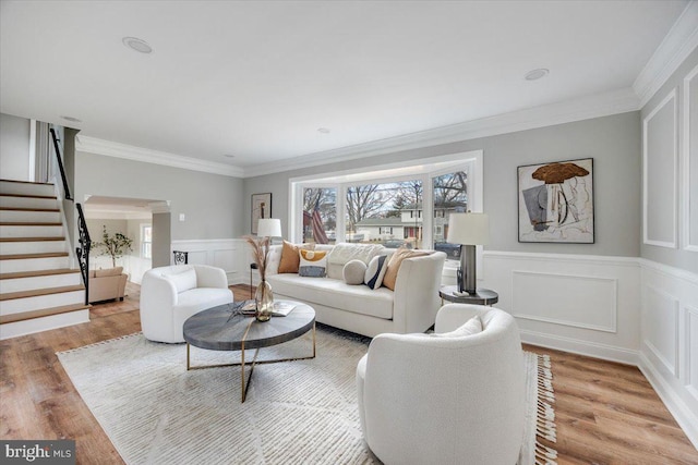 living area featuring light wood-type flooring, plenty of natural light, ornamental molding, and stairs