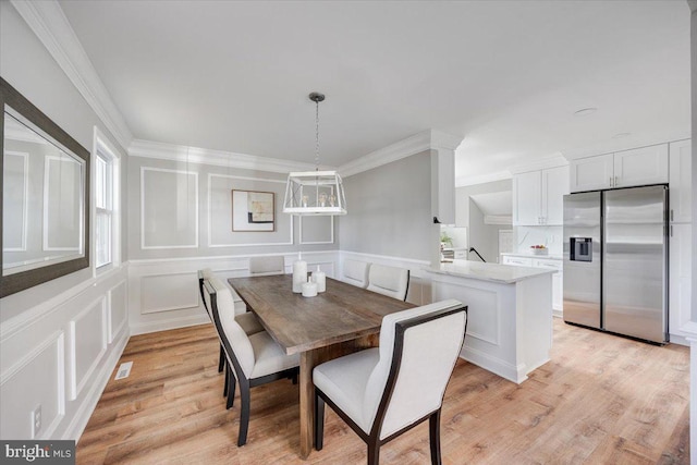 dining area featuring visible vents, light wood-style floors, crown molding, and a decorative wall