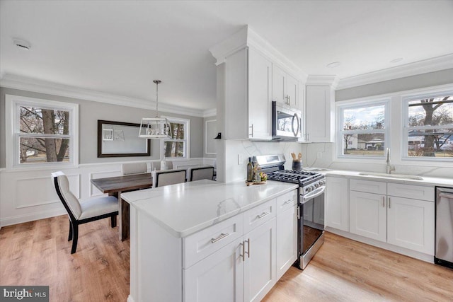 kitchen with a sink, stainless steel appliances, ornamental molding, and white cabinetry