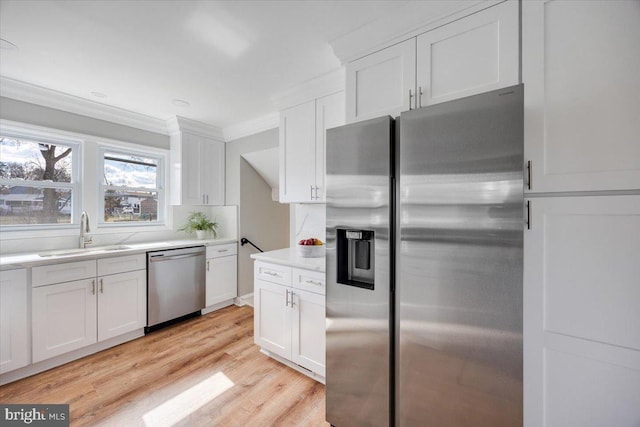 kitchen with white cabinetry, ornamental molding, appliances with stainless steel finishes, and a sink