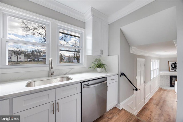 kitchen with ornamental molding, a sink, stainless steel dishwasher, white cabinets, and a fireplace