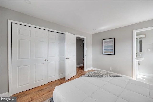 bedroom featuring light wood-type flooring, baseboards, a closet, and ensuite bathroom