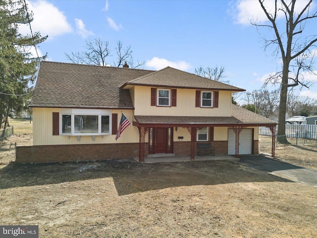 split level home with a porch, fence, roof with shingles, a garage, and brick siding