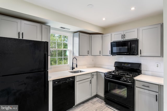 kitchen featuring visible vents, black appliances, gray cabinetry, a sink, and tasteful backsplash