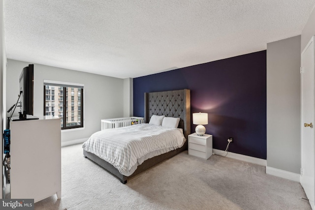 carpeted bedroom featuring a textured ceiling, an accent wall, and baseboards