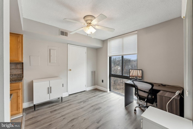 home office with baseboards, visible vents, ceiling fan, light wood-style floors, and a textured ceiling