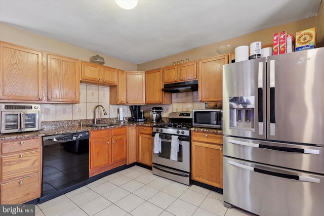 kitchen featuring under cabinet range hood, a sink, stainless steel appliances, dark stone counters, and decorative backsplash