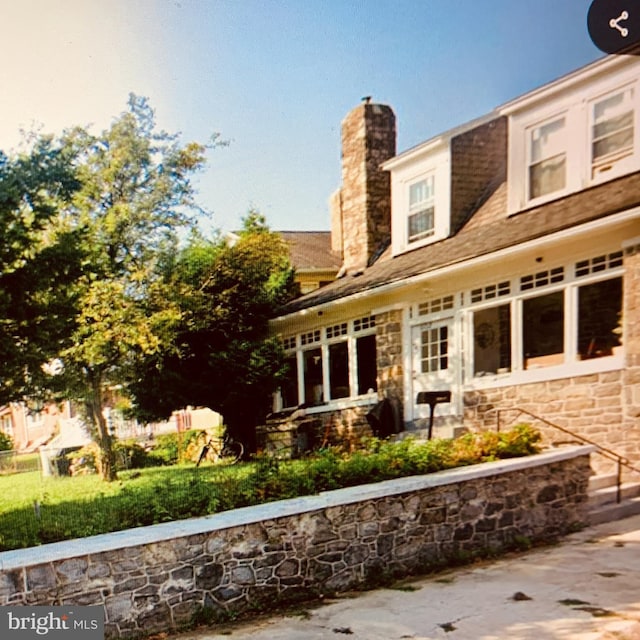 back of house featuring stone siding and a chimney