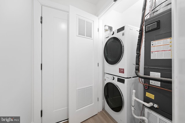 washroom featuring stacked washer / drying machine, laundry area, visible vents, and wood finished floors