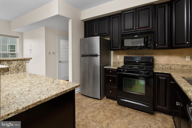 kitchen with dark cabinetry, black appliances, light stone countertops, and backsplash