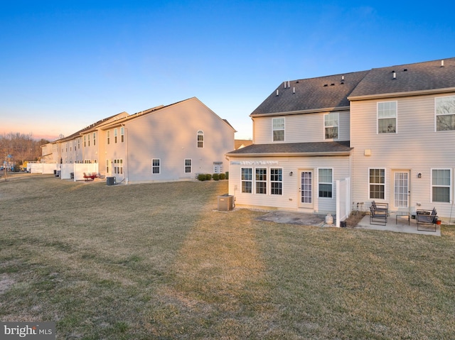 rear view of house featuring central air condition unit, a yard, a shingled roof, and a patio area