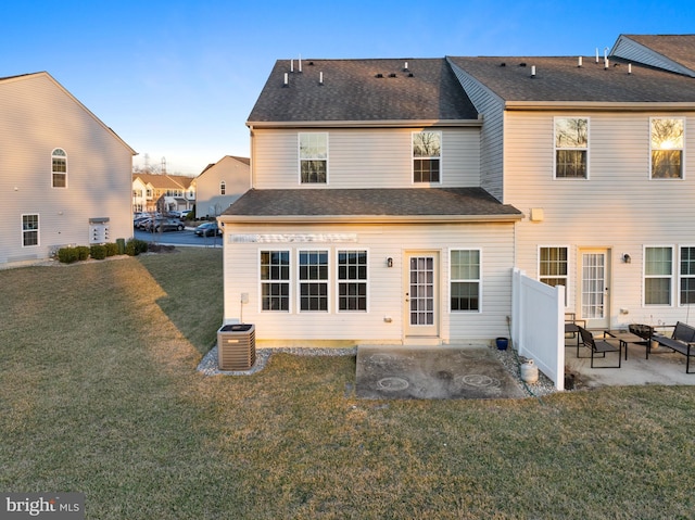 back of property with a yard, central AC unit, a shingled roof, and a patio