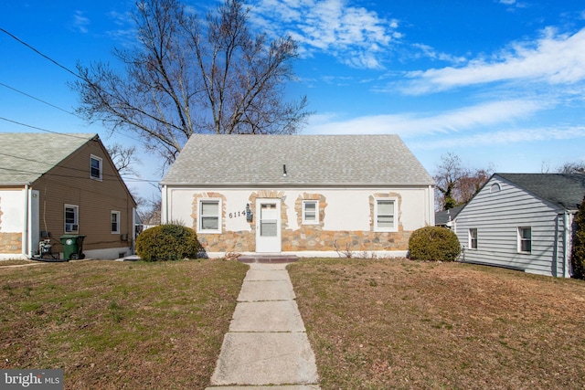 view of front of house featuring a front yard, stone siding, and roof with shingles