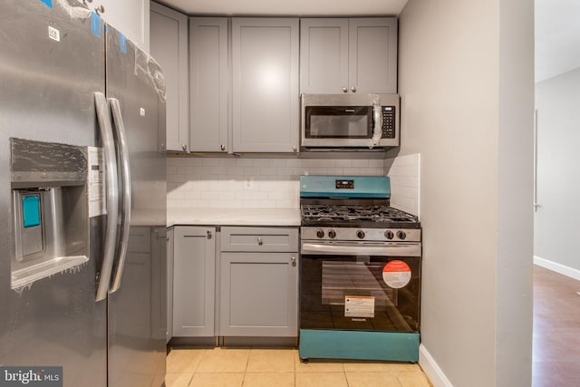 kitchen with tasteful backsplash, gray cabinets, light countertops, appliances with stainless steel finishes, and light tile patterned flooring