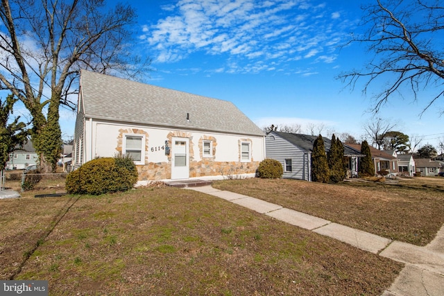 view of front of home with stone siding, roof with shingles, fence, and a front yard