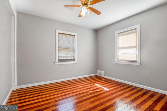 unfurnished room with a ceiling fan, wood-type flooring, visible vents, and baseboards