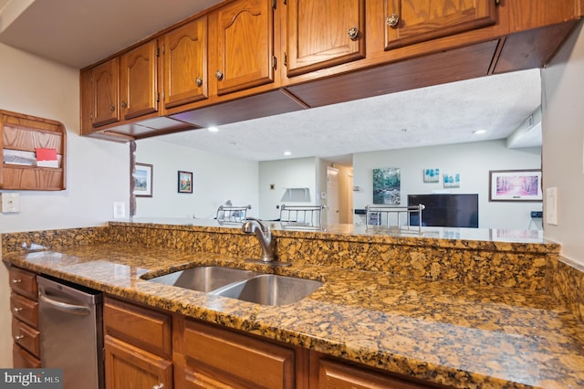 kitchen featuring brown cabinetry, a textured ceiling, dark stone counters, and a sink