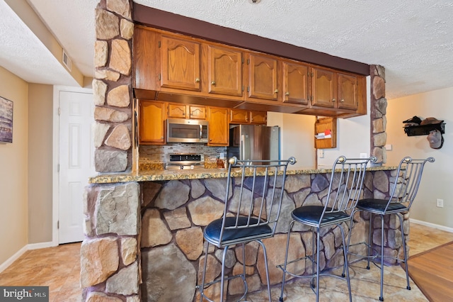 kitchen with brown cabinets, stone countertops, stainless steel appliances, and a peninsula