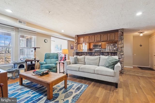 living area with light wood-type flooring, visible vents, baseboards, and a textured ceiling