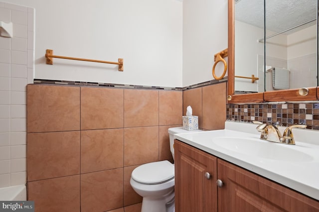 bathroom featuring vanity, a wainscoted wall, a textured ceiling, tile walls, and toilet