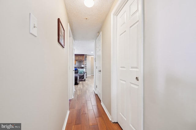 hall featuring wood finished floors, baseboards, and a textured ceiling