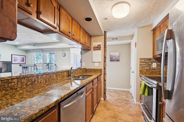 kitchen featuring brown cabinets, a sink, dark stone countertops, stainless steel appliances, and decorative backsplash