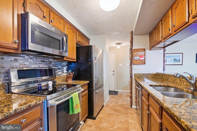 kitchen featuring backsplash, dark stone counters, brown cabinetry, stainless steel appliances, and a sink