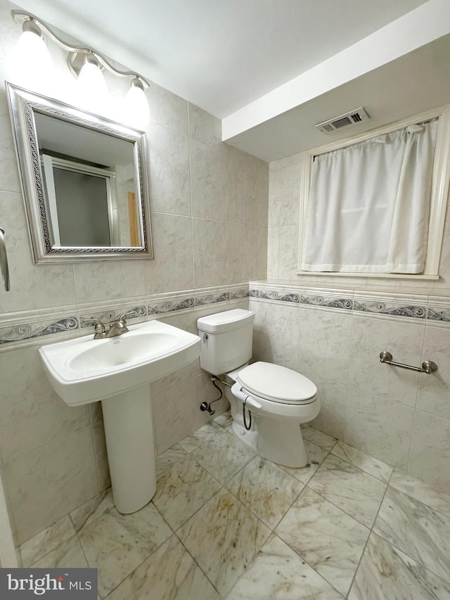 bathroom featuring toilet, marble finish floor, visible vents, and tile walls