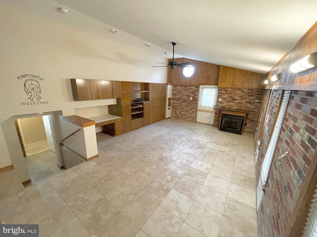 unfurnished living room featuring wooden walls, a ceiling fan, brick wall, a fireplace, and high vaulted ceiling