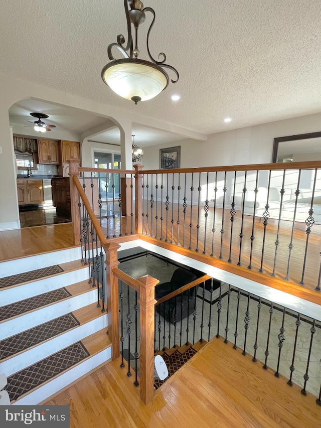 staircase with a chandelier, arched walkways, a textured ceiling, and wood finished floors