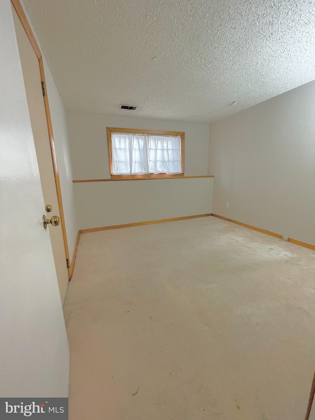 empty room with a textured ceiling, light carpet, visible vents, and baseboards