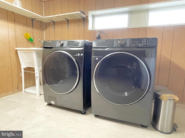 laundry room featuring light tile patterned floors, laundry area, wood walls, and independent washer and dryer