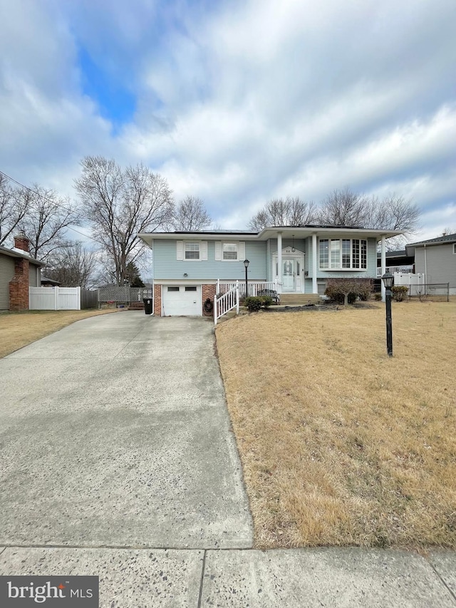 view of front facade with driveway, covered porch, fence, a front yard, and brick siding