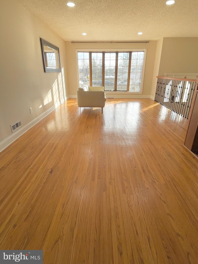 unfurnished living room featuring a wealth of natural light, a textured ceiling, visible vents, and wood finished floors