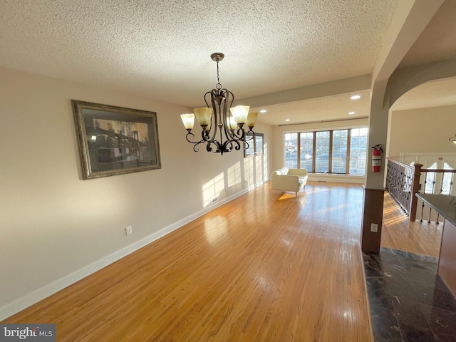 unfurnished dining area featuring arched walkways, a textured ceiling, baseboards, and wood finished floors