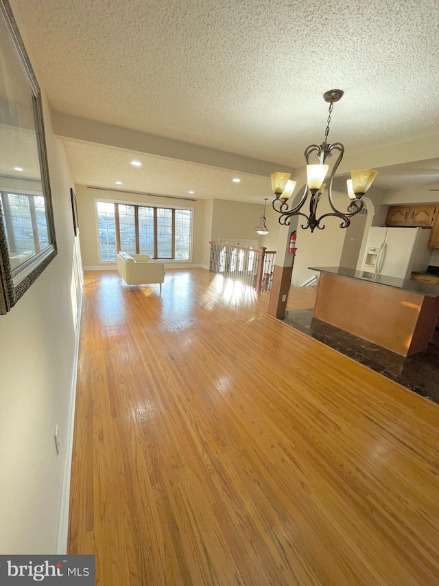 interior space with a chandelier, a textured ceiling, baseboards, and wood finished floors