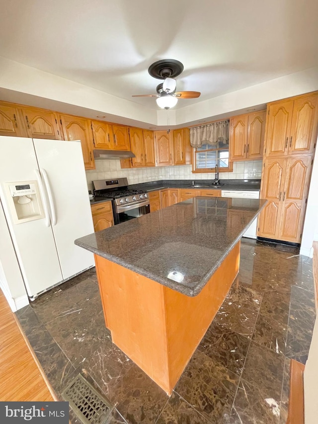 kitchen with gas range, tasteful backsplash, white refrigerator with ice dispenser, and under cabinet range hood