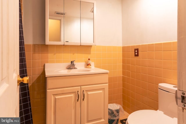 bathroom with toilet, visible vents, vanity, and tile walls