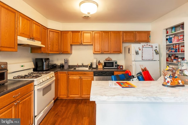 kitchen featuring stainless steel appliances, brown cabinetry, dark wood-type flooring, a sink, and under cabinet range hood