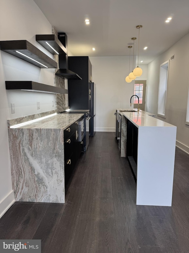 kitchen with dark cabinets, freestanding refrigerator, stainless steel stove, and wall chimney range hood