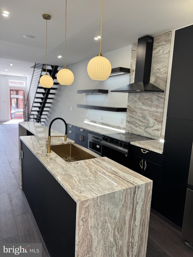 kitchen with wall chimney exhaust hood, dark cabinetry, a sink, and dark wood finished floors