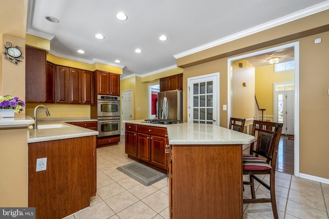 kitchen with ornamental molding, a sink, a kitchen breakfast bar, stainless steel appliances, and light tile patterned flooring