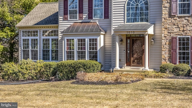 entrance to property featuring roof with shingles, a standing seam roof, stone siding, a lawn, and metal roof