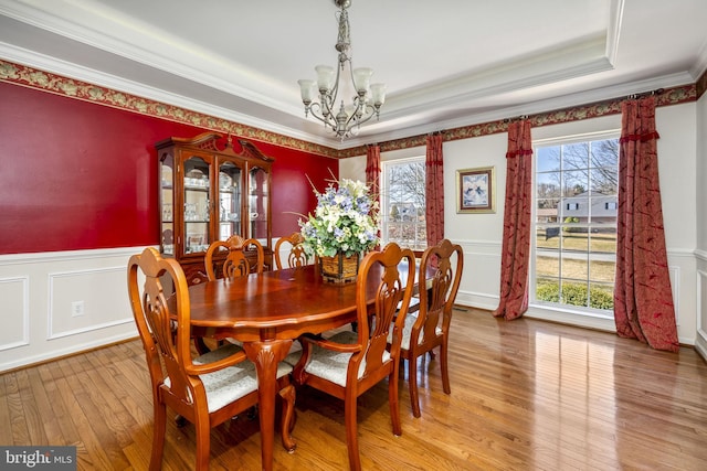 dining room featuring a wainscoted wall, ornamental molding, a tray ceiling, light wood finished floors, and a chandelier