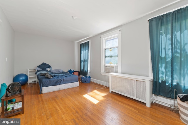 bedroom featuring cooling unit, radiator heating unit, baseboards, and hardwood / wood-style floors