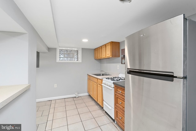 kitchen with baseboards, white gas range oven, light tile patterned floors, freestanding refrigerator, and a sink
