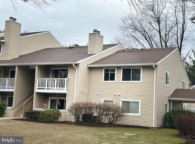 back of property with a shingled roof, stairs, a lawn, and a chimney