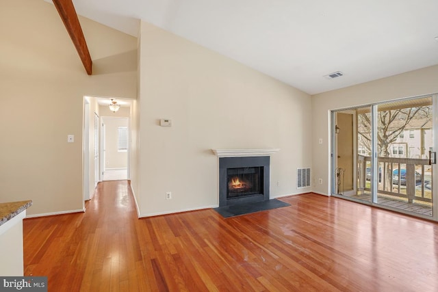 unfurnished living room featuring visible vents, a fireplace with flush hearth, vaulted ceiling with beams, and light wood finished floors