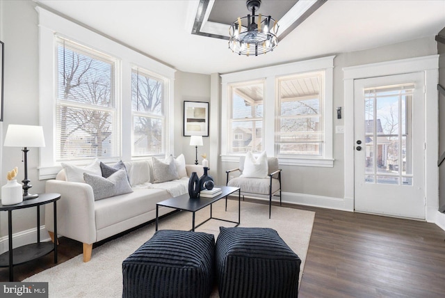 living area featuring an inviting chandelier, a raised ceiling, baseboards, and wood finished floors