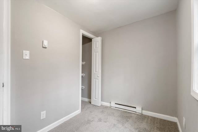 spare room featuring a baseboard heating unit, carpet, and baseboards